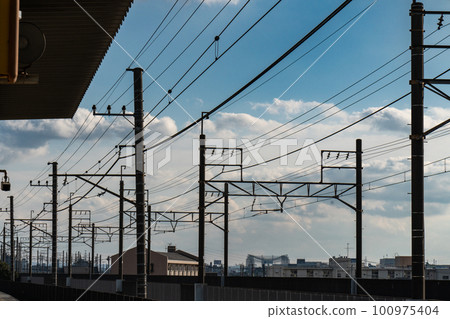 A blue sky with clouds spreading beyond the overhead wires of the railway 100975404