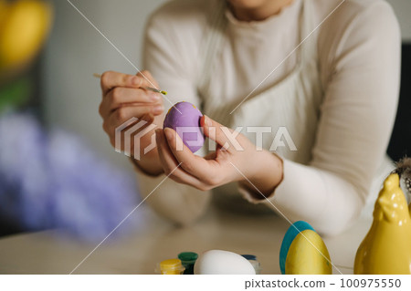 Middle selection of young woman painting Easter eggs in the kitchen. Spring holidays. 100975550