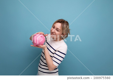 horizontal photo of an attractive young woman in a casual outfit with a piggy bank of coins on a horizontal photo of an attractive young woman in a casual outfit with a piggy bank of coins on a 100975560