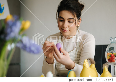 Attractive young woman painting Easter eggs in the kitchen. Spring holidays. Attractive young woman painting Easter eggs in the kitchen. Spring holidays. 100975561