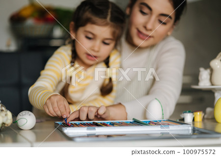 Happy laughing little girl painting picture with mom at the table in the kitchen. Easter holiday. Spring time Happy laughing little girl painting picture with mom at the table in the kitchen. Easter holiday. Spring time 100975572