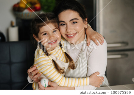 Close-up portrait of daughter with mom on kitchen. Beautiful girls dressed in apron Close-up portrait of daughter with mom on kitchen. Beautiful girls dressed in apron 100975599