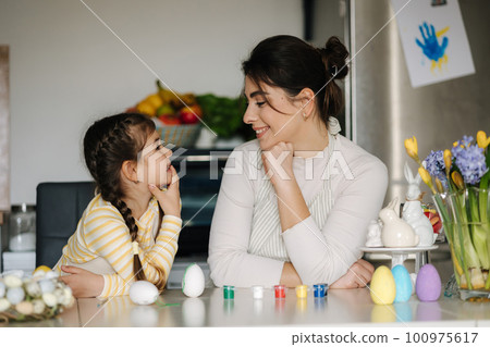 Cute little girl with her mother preparing for painting easter eggs. Mom and daughter look to each other 100975617