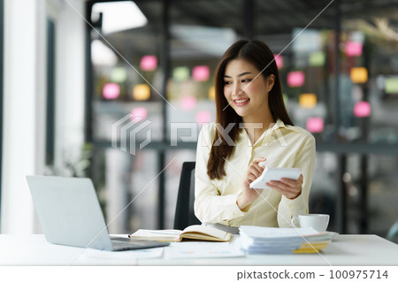 Beautiful Asian Banker or Accountant makes financial report and tax, analyzes profits. Accountant checks status of financial 100975714
