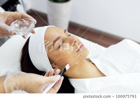 Beauty master applies a rejuvenating mask to the clients face. 100975791