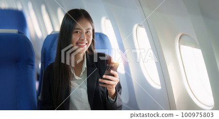 Beautiful Asian business woman chatting with client by mobile phone during flight. working, travel, business concept 100975803