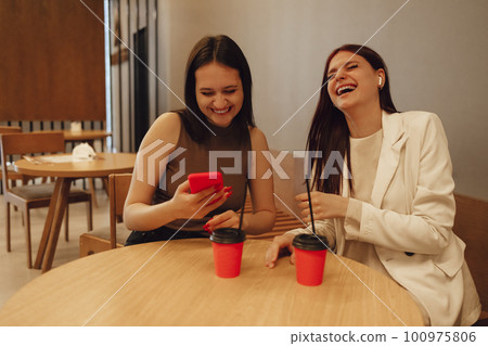 Female friends drink coffee or tea from red cups with straws. 100975806