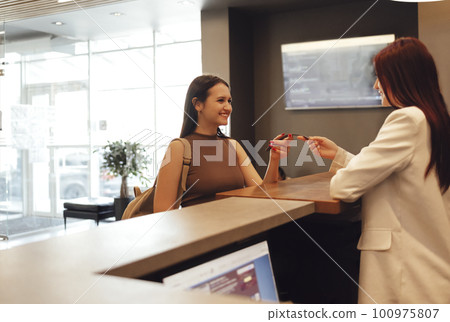 Woman in sportswear taking the sport bracelet while standing in front of window at gym at reception area Woman in sportswear taking the sport bracelet while standing in front of window at gym at reception area 100975807