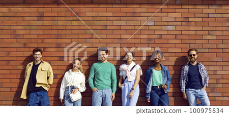 Diverse group of happy young men and women in casual clothes standing by street wall 100975834