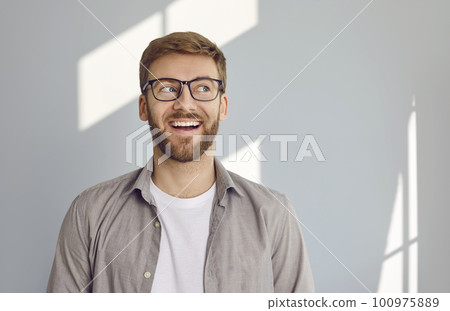 Portrait of smiling bearded man looking to the side on grey wall background. 100975889