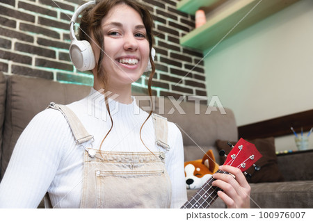 Smiling woman writing new blog content, playing ukulele guitar, explaining how to play, staying at home during lockdown and quarantine. Online learning, hobby Smiling woman writing new blog content, playing ukulele guitar, explaining how to play, staying at home during lockdown and quarantine. Online learning, hobby 100976007