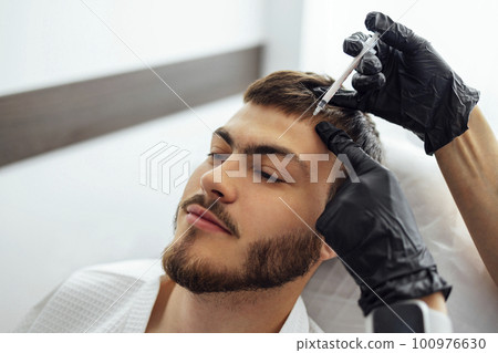 Female cosmetologist in transparent gloves makes an injection in the lower jaw of her client 100976630