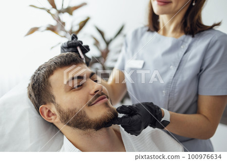 Female cosmetologist in transparent gloves makes an injection in the lower jaw of her client 100976634