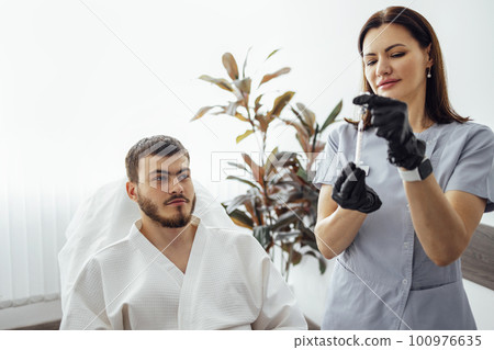 Female cosmetologist in transparent gloves makes an injection in the lower jaw of her client 100976635