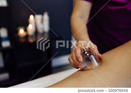 Faceless masseur rubbing back of customer with help of rubber vacuum cup working in salon Faceless masseur rubbing back of customer with help of rubber vacuum cup working in salon 100976648