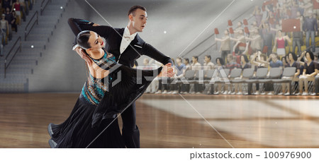 Graceful dancer. Young artistic man and woman in beautiful stage costumes dancing ballroom dance at stage under spotlights. Competition. 3D audience background Graceful dancer. Young artistic man and woman in beautiful stage costumes dancing ballroom dance at stage under spotlights. Competition. 3D audience background 100976900