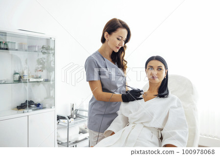 Beautiful caucasian young woman is doing a mole removal procedure in a modern beauty cosmetic dermatological clinic Beautiful caucasian young woman is doing a mole removal procedure in a modern beauty cosmetic dermatological clinic 100978068