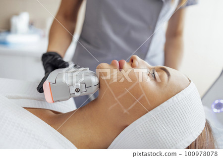 Portrait of relaxed young female client getting SMAS ultrasound face lifting massage 100978078