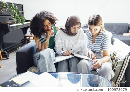 Three cute teenage girls do their homework. Caucasian, African American and a Muslim 100978079