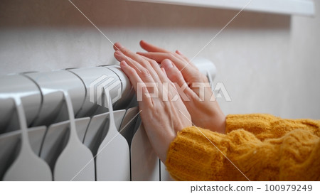 Women's hands are trying to keep warm on an aluminum radiator. 100979249