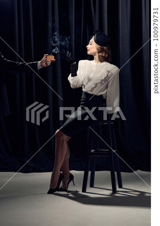 Charming woman wearing costume sitting on chair and smoking with calm face over dark background 100979731