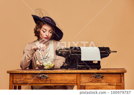 Sad pretty woman sitting at typewriter with sad face and eating salad over beige background 100979787