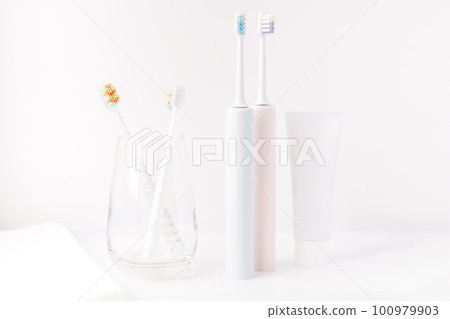Children's toothbrushes in glass cup and electric toothbrushes against white background Children's toothbrushes in glass cup and electric toothbrushes against white background 100979903
