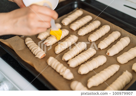 Man greases sausages in dough on baking sheet with parchment paper 100979907