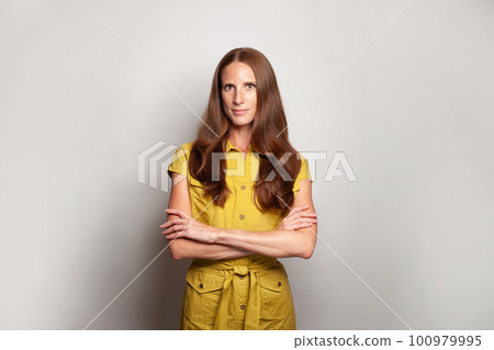 Pretty elegant woman with long ginger hair looking at camera and standing with arms crossed Pretty elegant woman with long ginger hair looking at camera and standing with arms crossed 100979995
