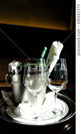 Wine glasses in a wine cooler with green bottles in the afternoon sun 100981373