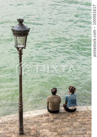 Couple of people sitting by the river Seine in Paris, France Couple of people sitting by the river Seine in Paris, France 100981617