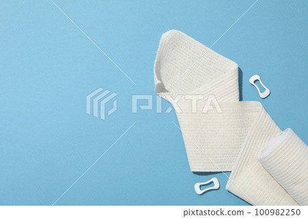 Concept of help during an injury, elastic bandage on blue background Concept of help during an injury, elastic bandage on blue background 100982250