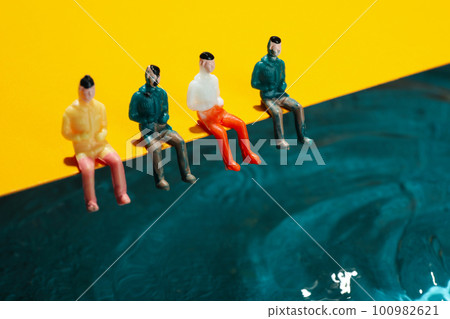 Toy people sitting on yellow background near water Toy people sitting on yellow background near water 100982621