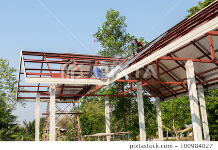 Roof repair, Construction worker installing new roof, roofing tools, power drill used on new roof with sheet metal. Roofing - construction worker standing on a roof covering it with metal. 100984027