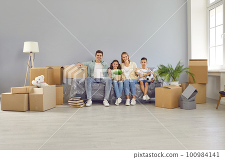 Happy family with children moving in new modern apartment house sitting on sofa looking at camera. 100984141
