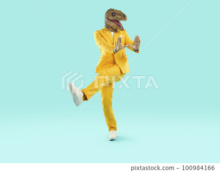 Happy man in a yellow suit and a funny dinosaur mask dancing on a blue studio background 100984166