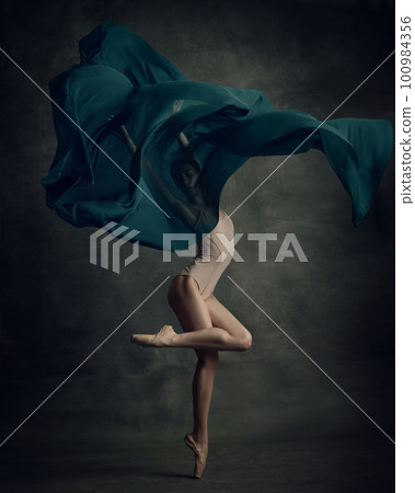 Shot of professional ballerina dancing in beige bodysuit with fabric isolated over dark green background 100984356
