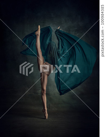 Young and incredibly beautiful ballerina standing in twine and holding silk fabric over dark green background 100984385