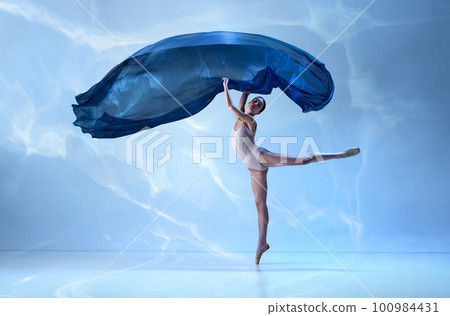 Graceful movements of one beautiful ballerina dancing with silk cloth isolated over blue background. Female dancer in ballet outfit Graceful movements of one beautiful ballerina dancing with silk cloth isolated over blue background. Female dancer in ballet outfit 100984431