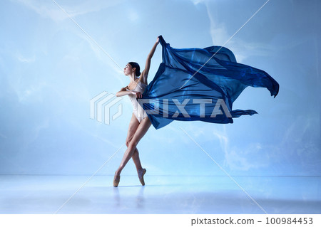 Beautiful ballerina wearing beige bodysuits emotional dancing with fabric silk over blue background Beautiful ballerina wearing beige bodysuits emotional dancing with fabric silk over blue background 100984453