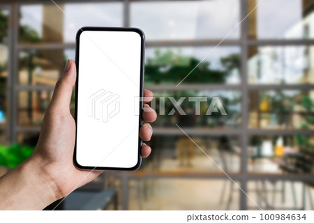 Mockup image of hand holding white mobile phone with blank white screen in cafe. 100984634