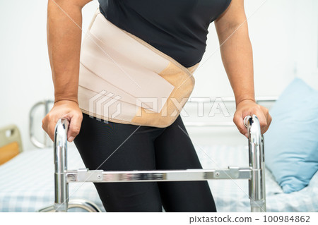Asian lady patient wearing back pain support belt for orthopedic lumbar with walker. Asian lady patient wearing back pain support belt for orthopedic lumbar with walker. 100984862