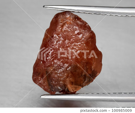 Natural gemstone red spessartine garnet on a gray background 100985009
