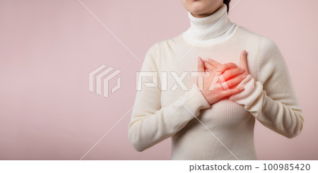 Young woman suffering from heart attack on light pink studio background. Painful cramps, Heart disease, Pressing on chest with painful expression. Healthcare world health day concept. Young woman suffering from heart attack on light pink studio background. Painful cramps, Heart disease, Pressing on chest with painful expression. Healthcare world health day concept. 100985420
