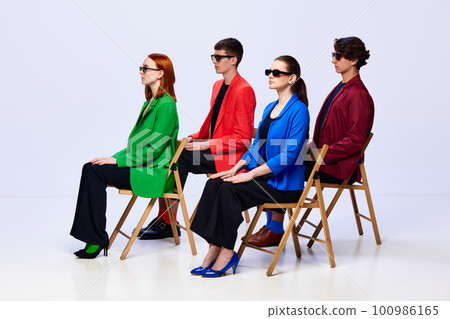 Group of young people, student wearing colorful stylish jackets sitting on chair and looking away over white background Group of young people, student wearing colorful stylish jackets sitting on chair and looking away over white background 100986165