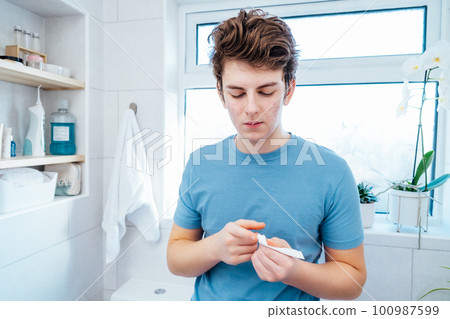 Concentrated caucasian teenage boy with acne problem take care his face skin at home. He looking in the mirror and aplying cream on the face in bathroom. Teenager skin care every day treatment process Concentrated caucasian teenage boy with acne problem take care his face skin at home. He looking in the mirror and aplying cream on the face in bathroom. Teenager skin care every day treatment process 100987599