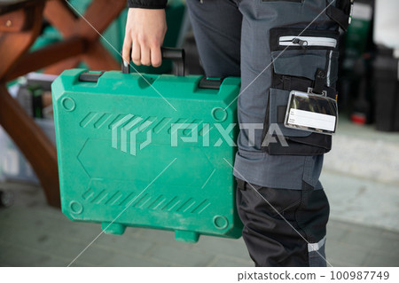 A girl in work pants holds a green tool case in her hand. A girl in work pants holds a green tool case in her hand. 100987749