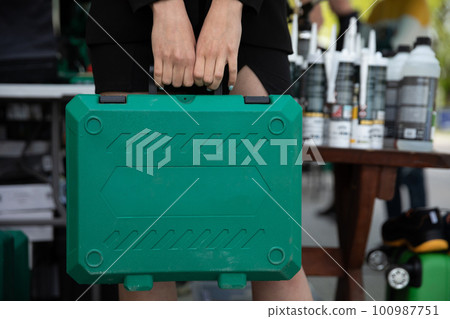 In the close-up frame, the girl holds a green tool case in her hands. 100987751