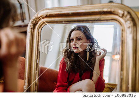 Young woman in elegant dress preparing for evening, looking in a mirror. Young woman in elegant dress preparing for evening, looking in a mirror. 100988039