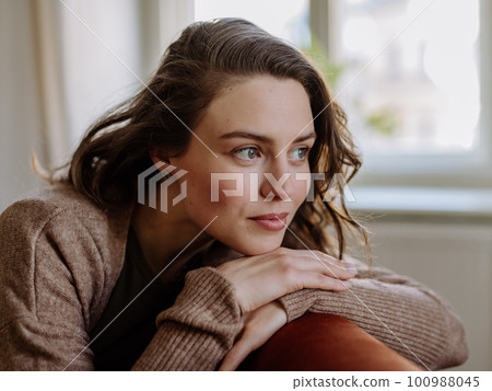 Portrait of young pensive woman, in her apartment. 100988045
